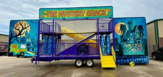 The Mystery Shack inflatable obstacle course rental with a spooky themed design, colorful artwork, and climbing structure displayed outdoors.
