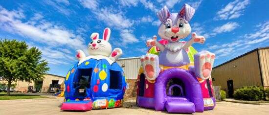 Colorful bunny-themed inflatable bounce houses with playful designs set up outdoors under a bright blue sky.