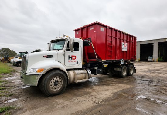 Red roll-off dumpster truck at an industrial service yard