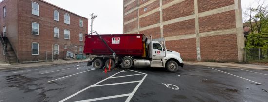 Roll-off dumpster truck parked beside a commercial brick building