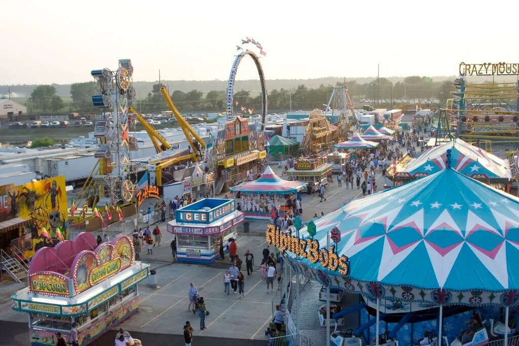 Busy carnival fairground with rides, food stands, and crowds enjoying the festivities.