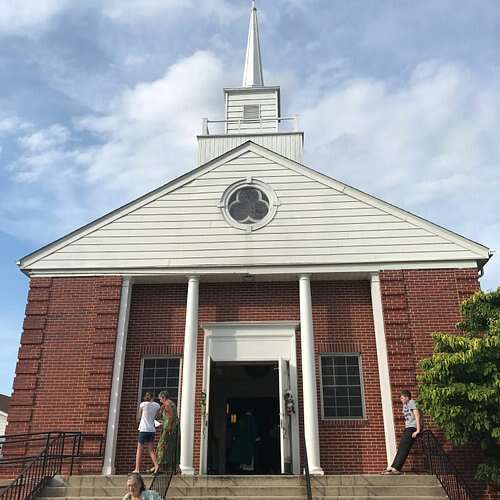 Front view of St. Edmond Catholic Church with visitors entering on a sunny day.
