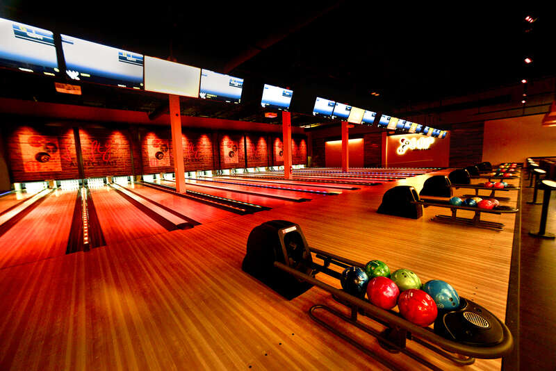 Modern indoor bowling alley with multiple lanes, colorful bowling balls, and overhead screens.