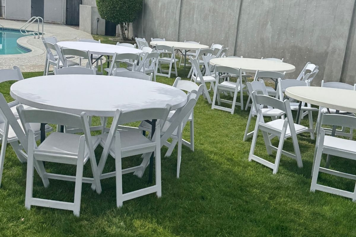 White resin chairs paired with 60-inch round tables set up on green grass for a backyard event near a pool in Phoenix AZ White resin chairs paired with 60-inch round tables set up on green grass for a backyard event near a pool in Phoenix AZ