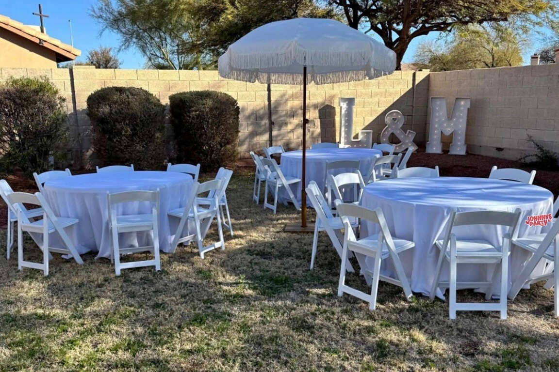 Round table with white resin chairs and black linen event setup