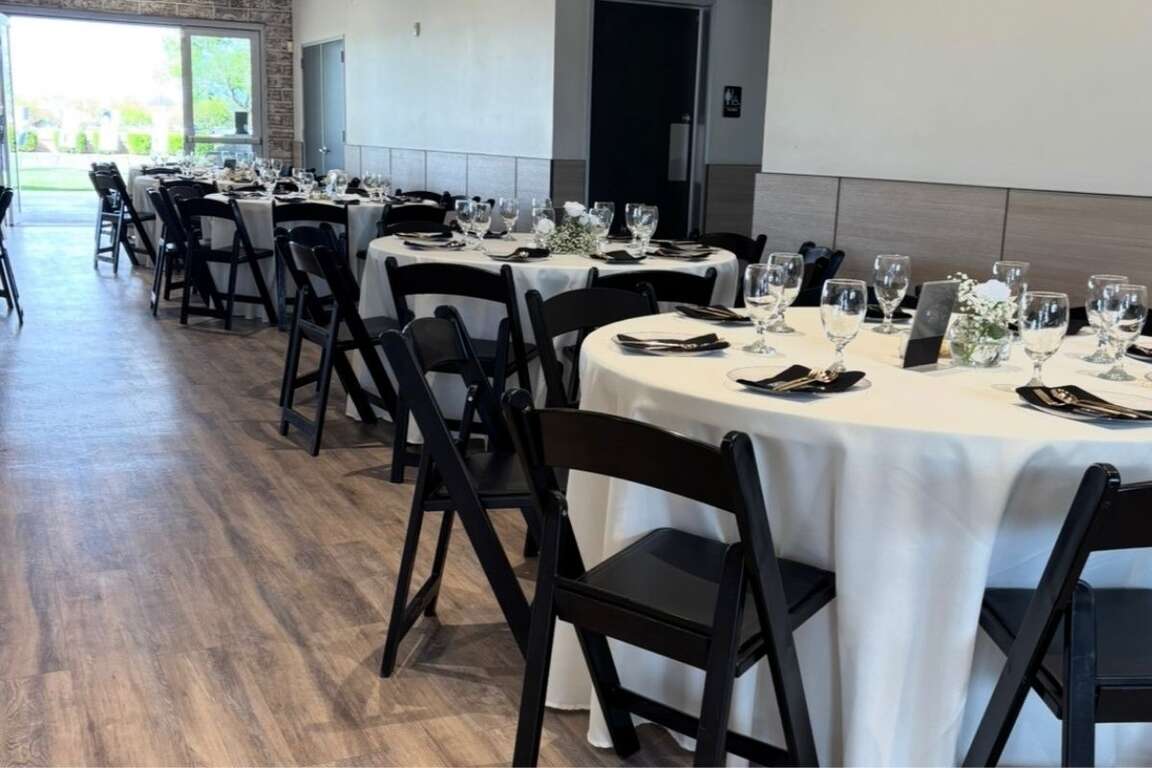 Round tables paired with black resin chairs set up in a venue for a reception