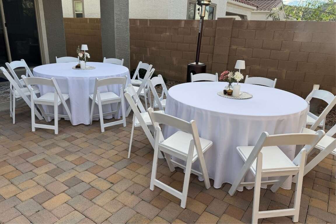 Round tables with white resin chairs and white tablecloths set up for an event in Glendale, Arizona