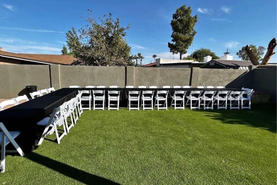 White resin chairs and 6 ft tables with black tablecloths set up in a backyard in Avondale, AZ