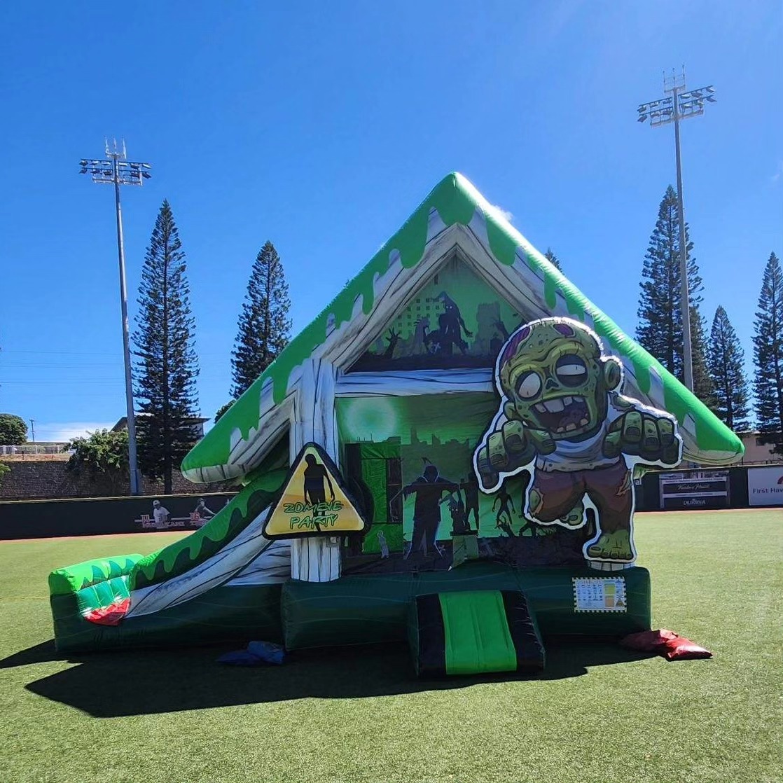 Zombie-themed inflatable bounce house slide with a prominent zombie figure at the entrance, set up on a sunny day with tall pine trees in the background, perfect for children