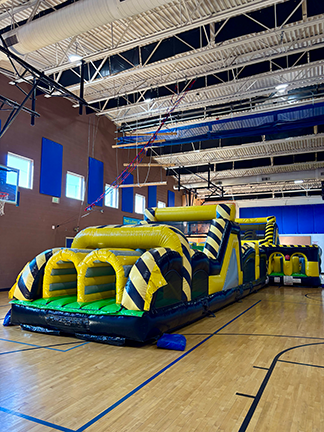 Big black nd yellow obstacle course with ramps and slides set up in a gym for kids to play on