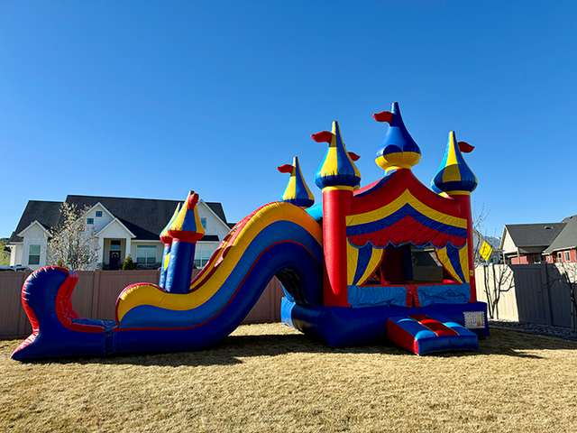 Colorful Bounce house with slide set up in a backyard in front of a clear blue sky