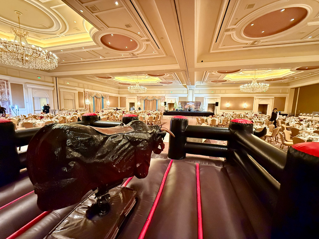 A Mechanical Bull set up in a ballroom with many tables and chairs around it as the main event.