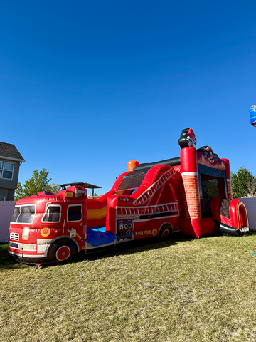 Red fire truck inflatable bounce house with slide set up in the backyard for a birthday party with a clear blue sky