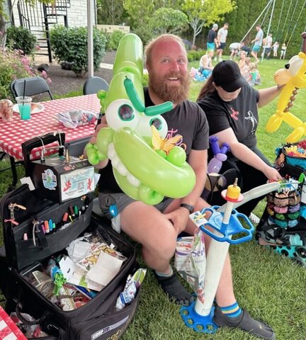 A man at a backyard party holding a green alligator made out of balloons on a sunny day.