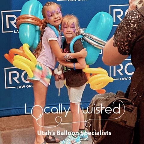 Two young girls smiling for a picture with fun backpacks made out of balloons.