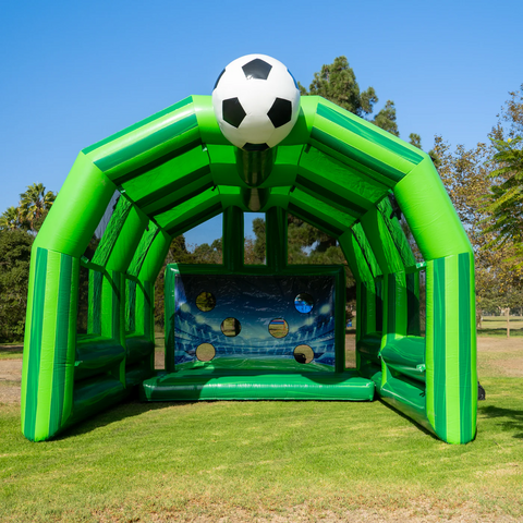 Large Green soccer game with a big white and block soccer ball on top under the sun.