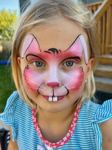 Young girl getting a princess-themed face paint design at a community festival.