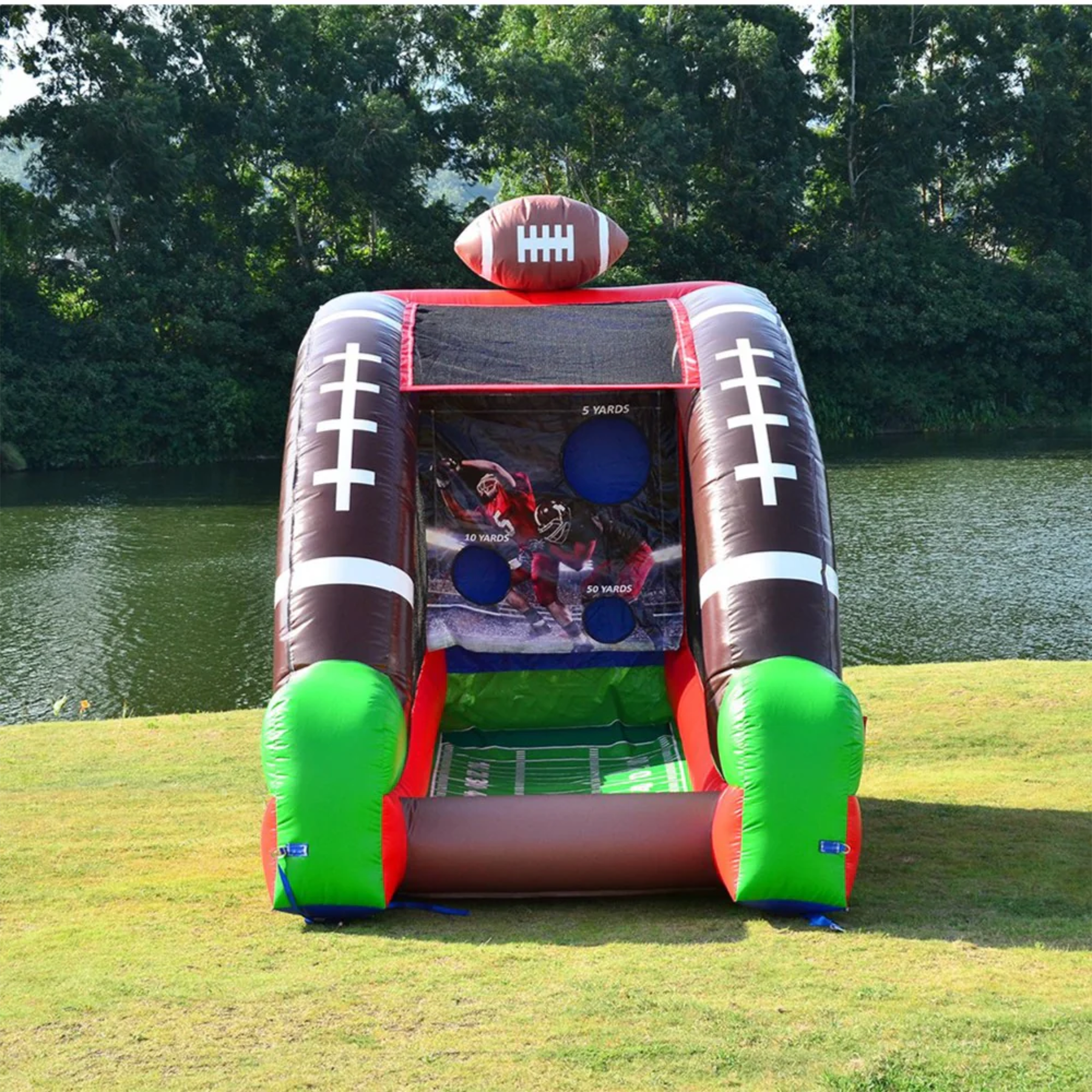 Inflatable Football game set up on grass in front of trees and water.