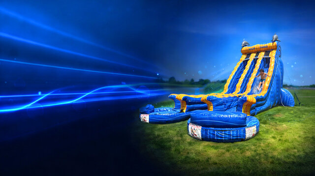 Towering blue and yellow inflatable water slide with a child sliding down into the splash pool, set on grass with dramatic neon light streaks