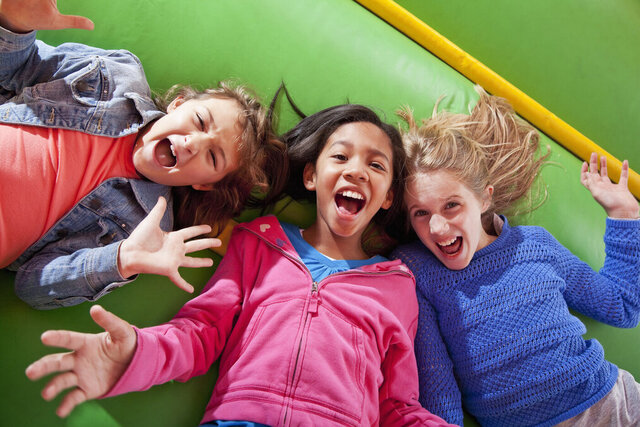 Three kids laughing while playing on a green inflatable