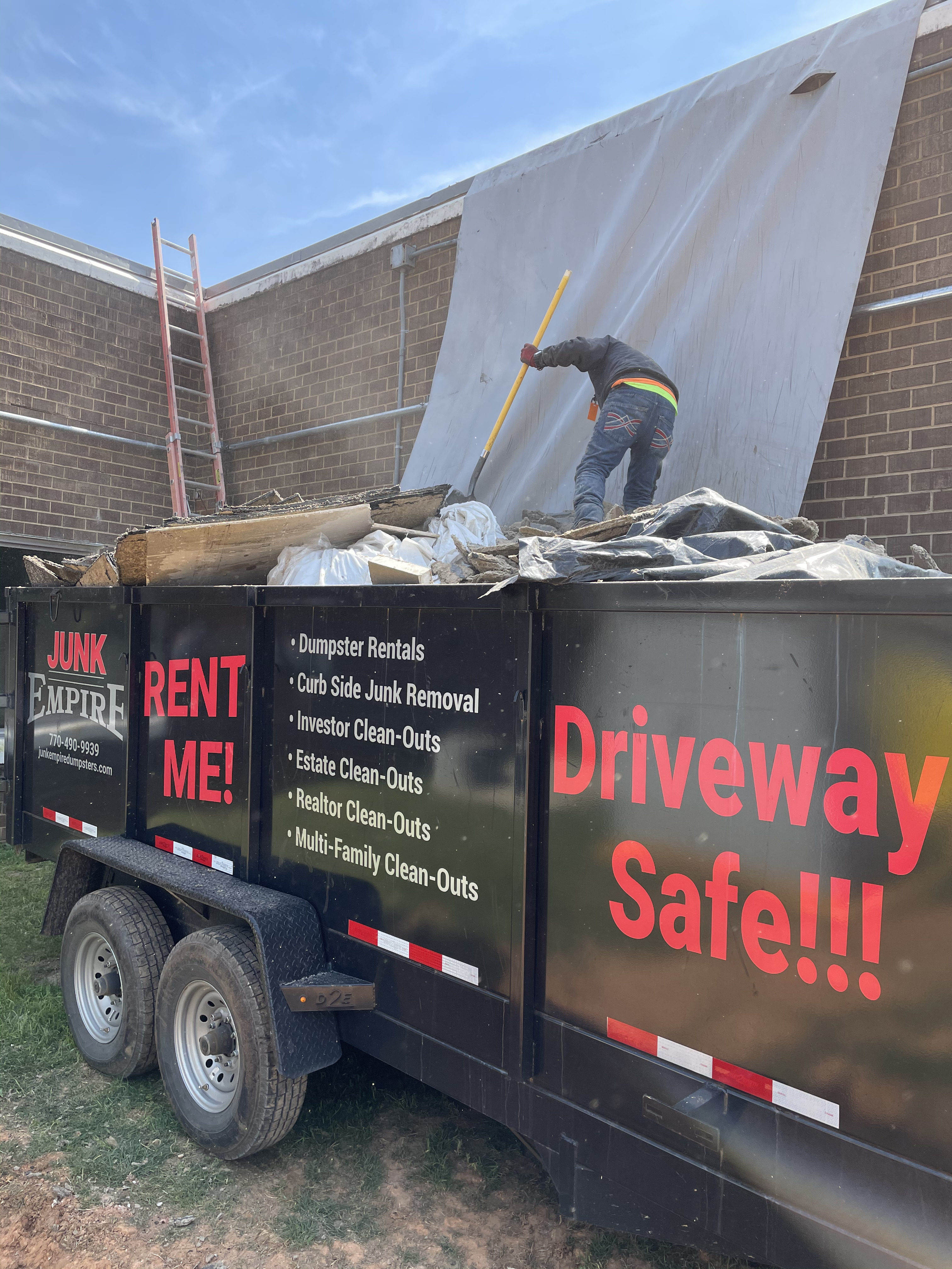 Junk Empire black dumpster filled with construction debris, worker shoveling material on top.