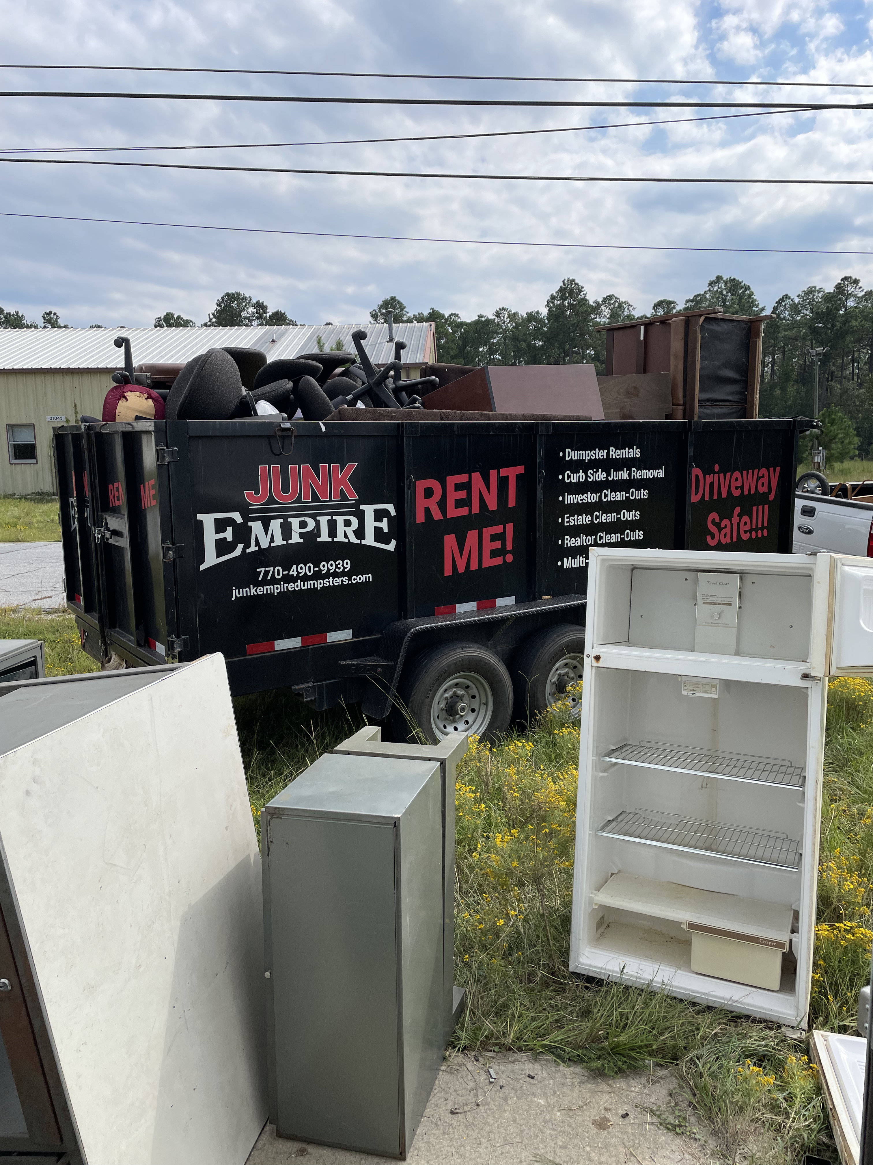 Junk Empire black dumpster loaded with old furniture and junk items, with appliances placed beside it.