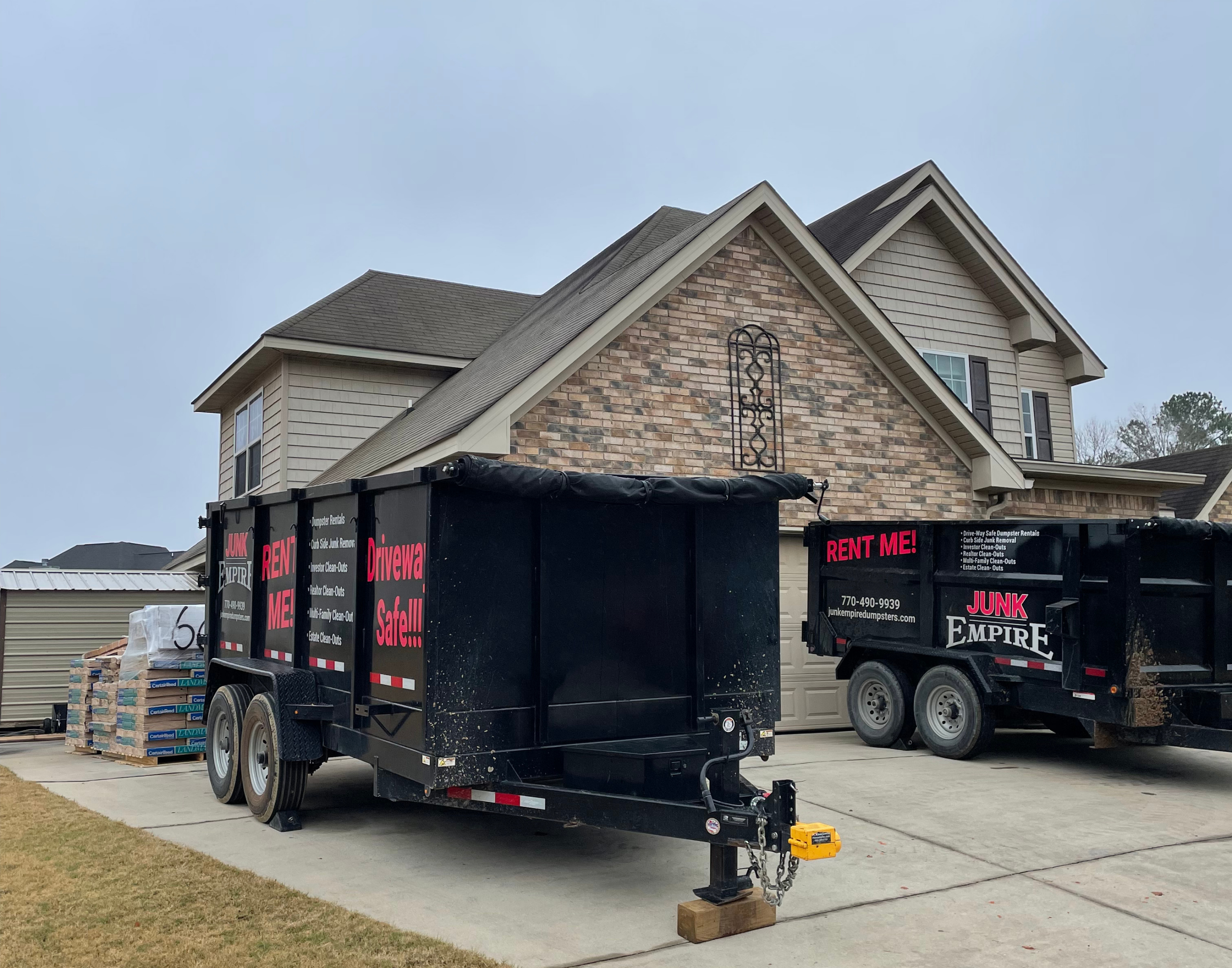 Junk Empire black dumpsters parked in a residential driveway for junk removal and dumpster rental services.