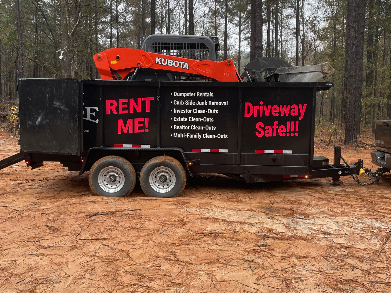 Junk Empire black dumpster with bold red RENT ME! and Driveway Safe!!! text, loaded with a Kubota machine for junk removal and clean-out services.