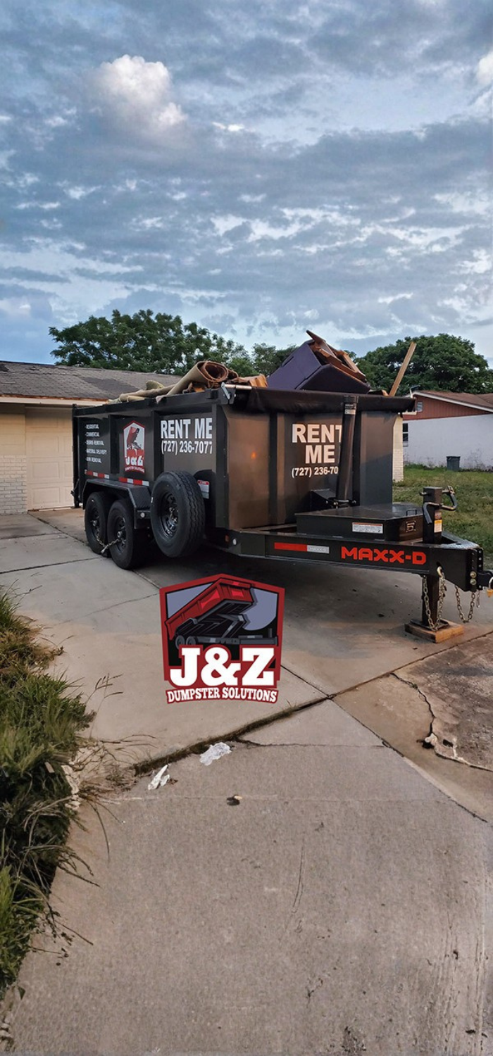 Black J&Z Dumpster Solutions trailer full of debris in a residential driveway. Black J&Z Dumpster Solutions trailer full of debris in a residential driveway.