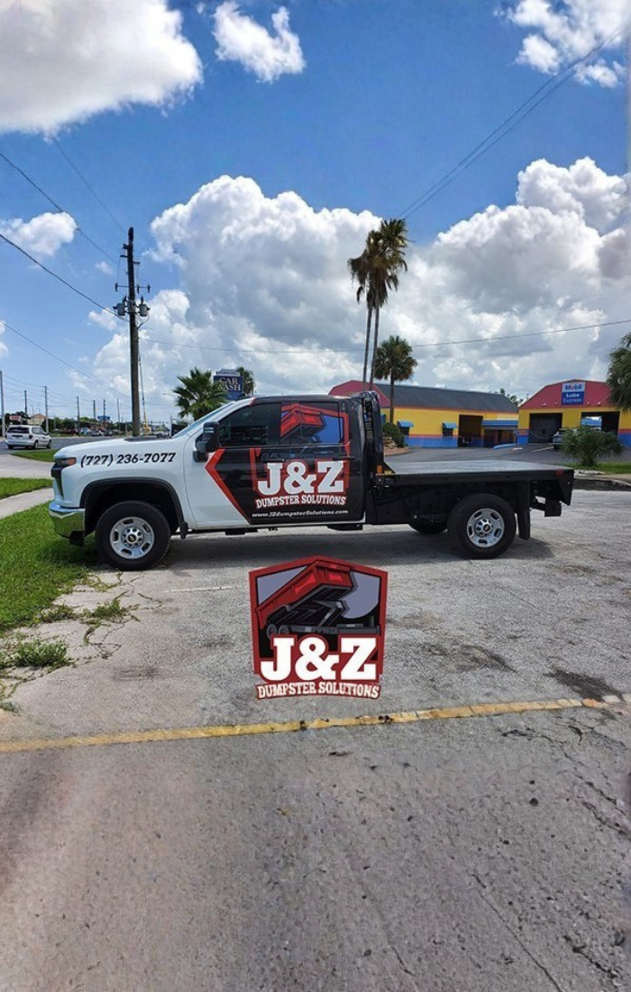 J&Z Dumpster Solutions flatbed truck in a commercial parking lot under palm trees. J&Z Dumpster Solutions flatbed truck in a commercial parking lot under palm trees.
