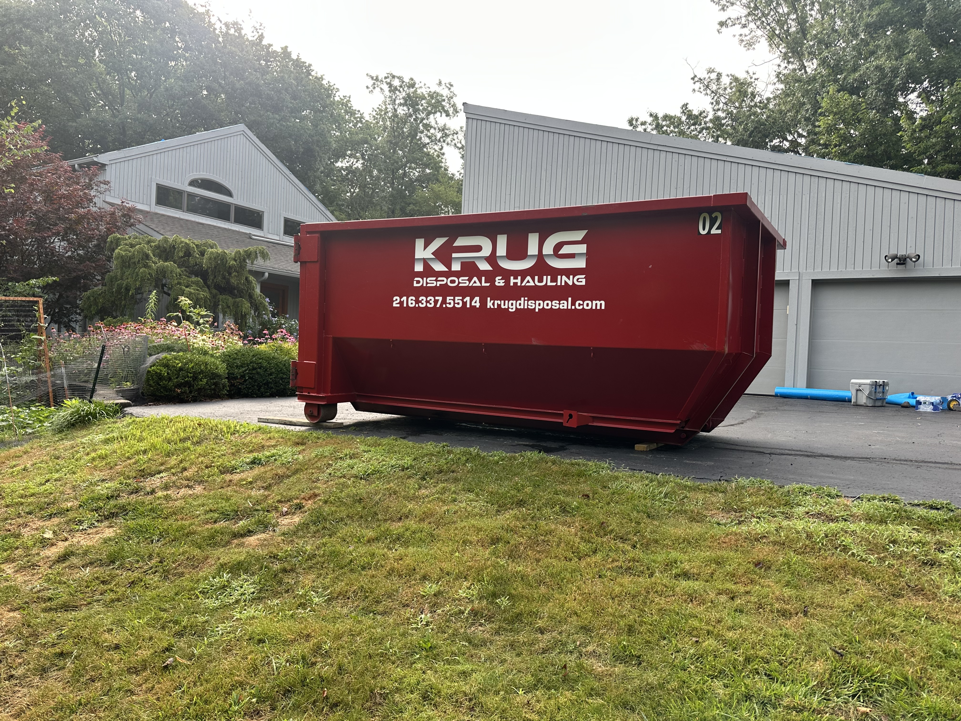Red residential dumpster from Krug Disposal in a front yard. Red residential dumpster from Krug Disposal in a front yard.
