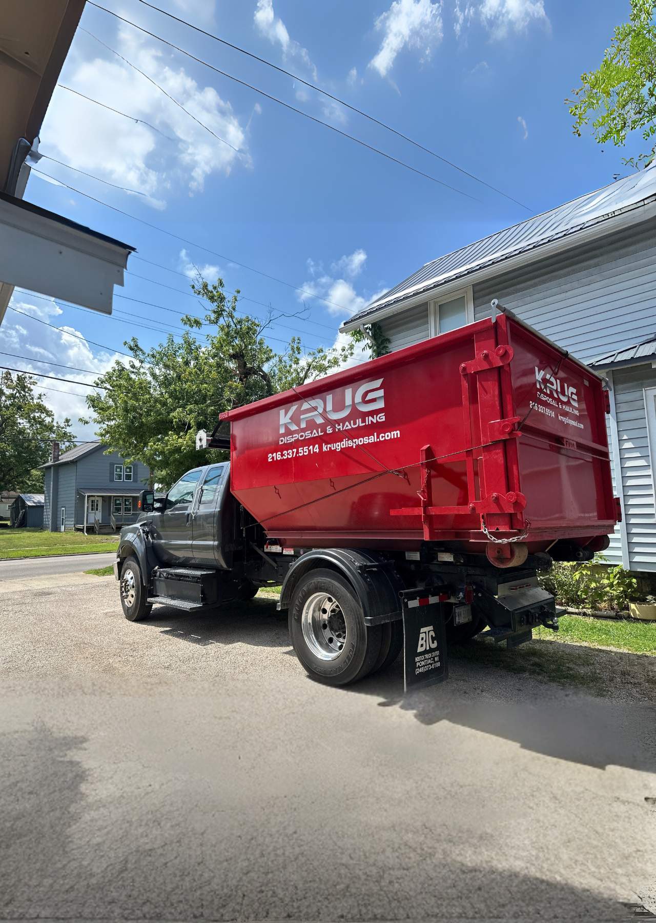 Krug Disposal red dumpster truck parked by a residential home.