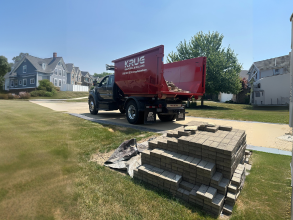 Krug Disposal & Hauling dumpster truck delivering near stacked paving stones