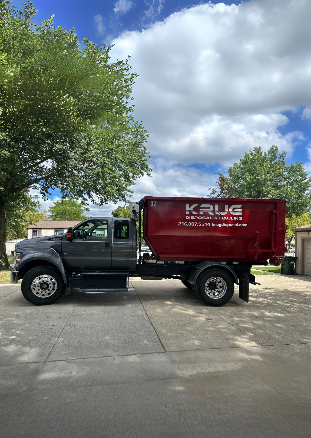 Krug Disposal red dumpster truck parked on a residential driveway.