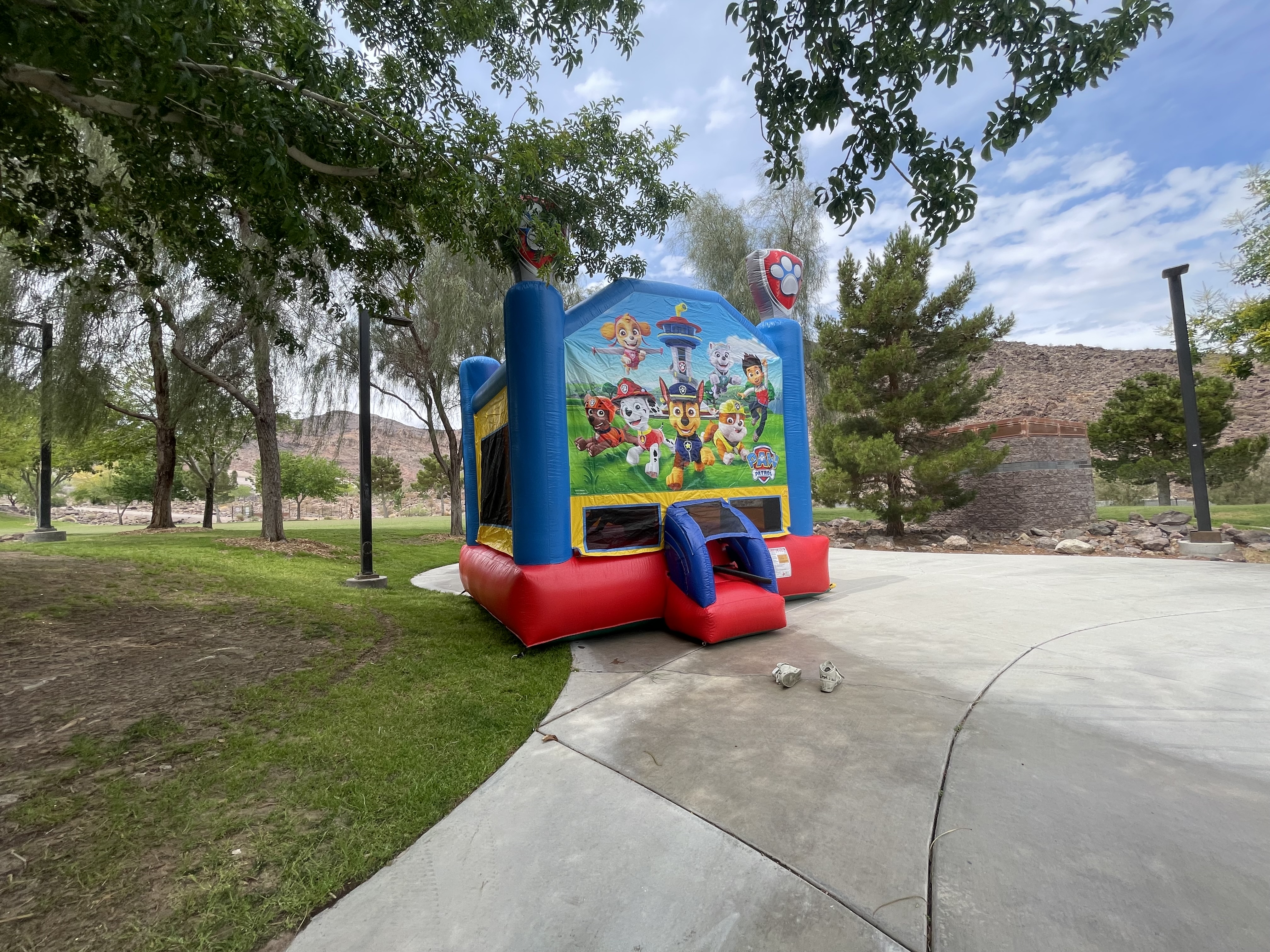 Bounce house featuring colorful Paw Patrol characters, set in a grassy park area with trees and a pathway, highlighting Liberty Party Jumpers LLC