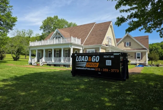 Load and Go Pros dumpster on a rural property lawn near a two-story farmhouse