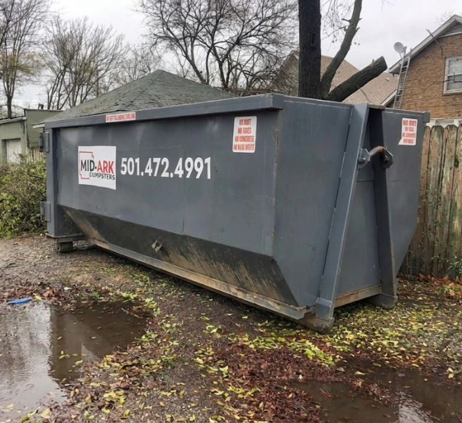 Roll-off dumpster rental on a residential driveway after rain, provided by Mid-Ark Dumpsters LLC