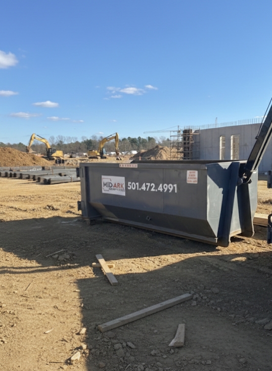 Construction site roll-off dumpster under a clear sky, hauled by Mid-Ark Dumpsters LLC