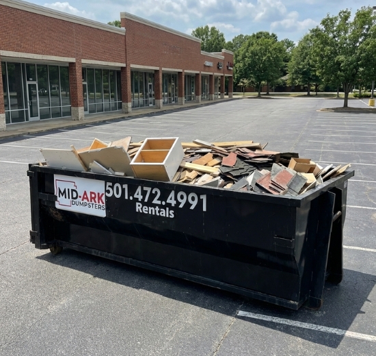 Loaded roll-off dumpster in a parking lot for cleanout waste hauling by Mid-Ark Dumpsters LLC