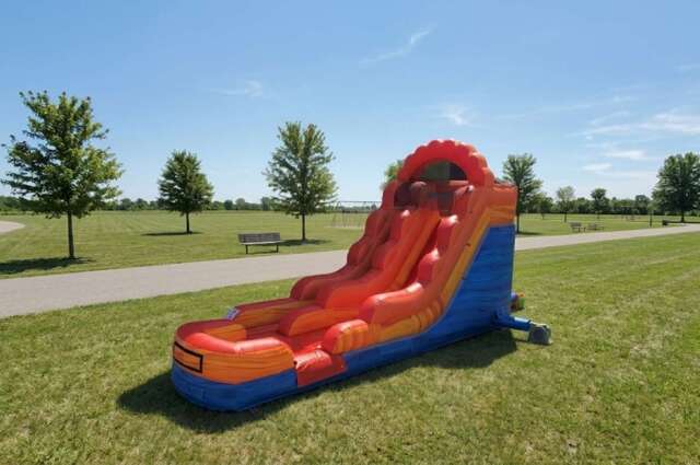 A large inflatable orange and red water slide set up on a green lawn with trees in the background