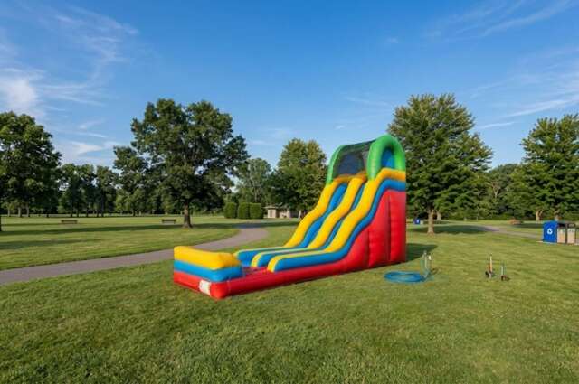 A colorful inflatable water slide with yellow and blue lanes on a grassy field under a clear blue sky