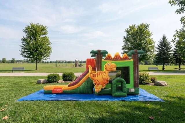 A colorful inflatable jungle-themed water slide and play structure set up on a blue tarp in a grassy yard