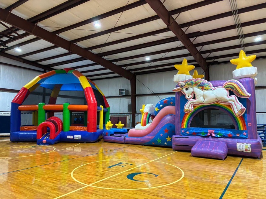 Two bounce houses and a unicorn slide set up indoors on a gym floor