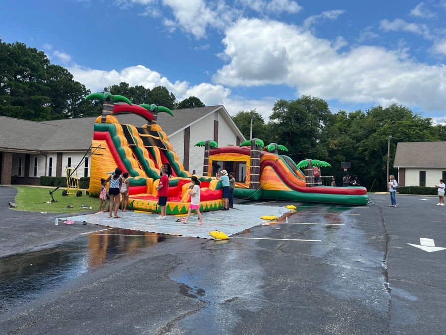 A water slide and combo bouncer set up in a church car park, with children lining up to climb in