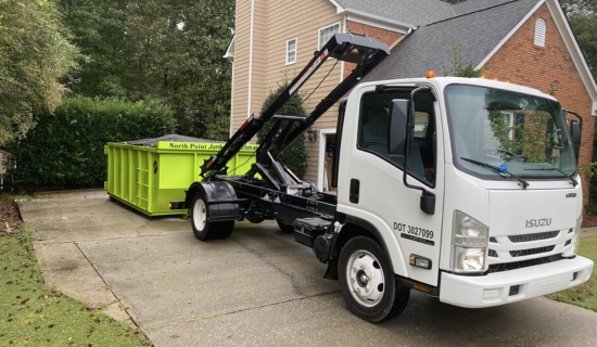 North Point Dumpsters Isuzu truck dropping off a lime-green roll-off container in a residential driveway