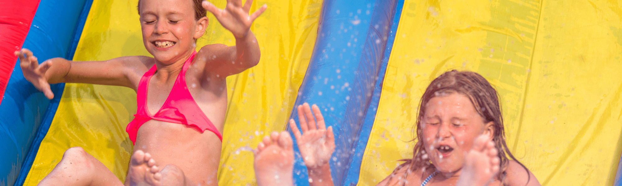 Kids splashing and sliding down a colorful inflatable water slide outdoors