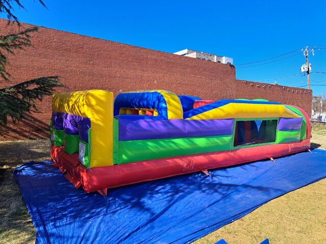 Extended rainbow inflatable obstacle course rental at a community event in Travelers Rest, SC, offering multiple challenge sections, tunnels, and open mesh viewing areas.
