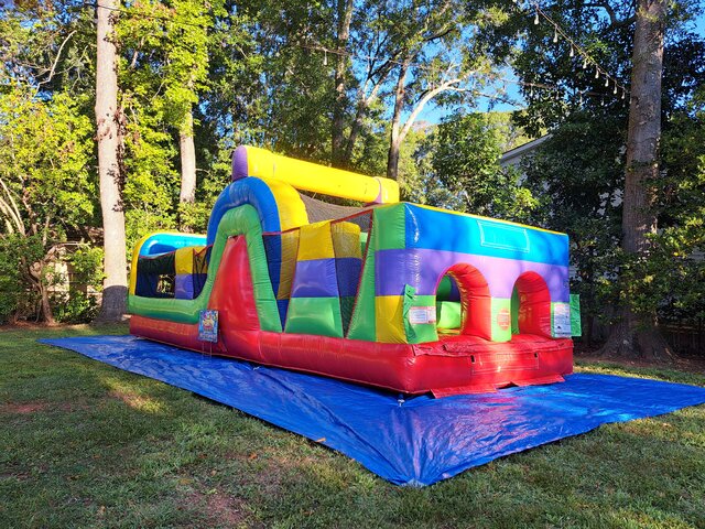 30-foot rainbow inflatable obstacle course rental at a backyard event in Travelers Rest, SC, designed with crawl-through tunnels and kid-friendly obstacle challenges.