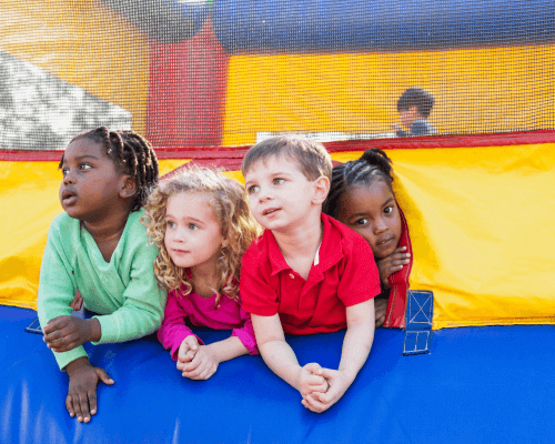 Three smiling kids peeking out from the entrance of a colorful bounce house, ready for fun and excitement. Book the best Bounce House Rentals in Greenville, SC for your next event!