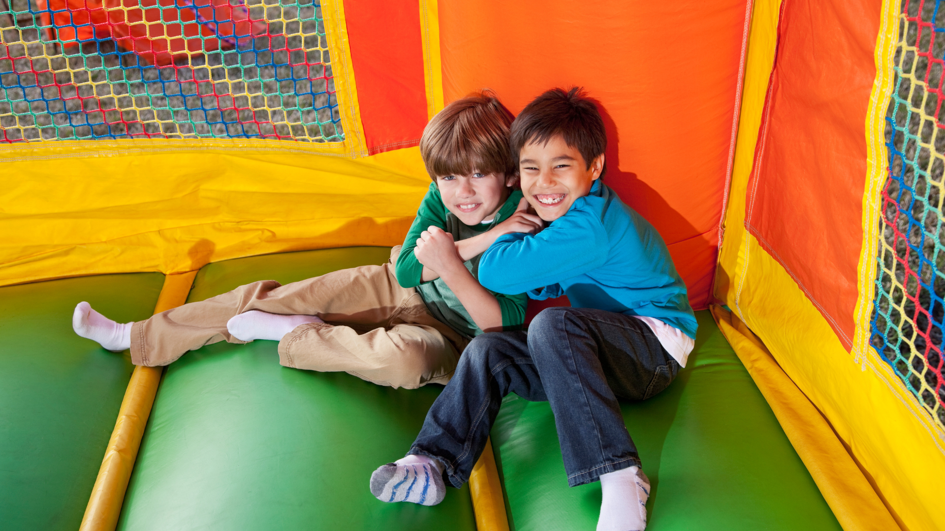 Two smiling boys playing together inside a colorful inflatable from bounce house rentals in Berea SC Two smiling boys playing together inside a colorful inflatable from bounce house rentals in Berea SC